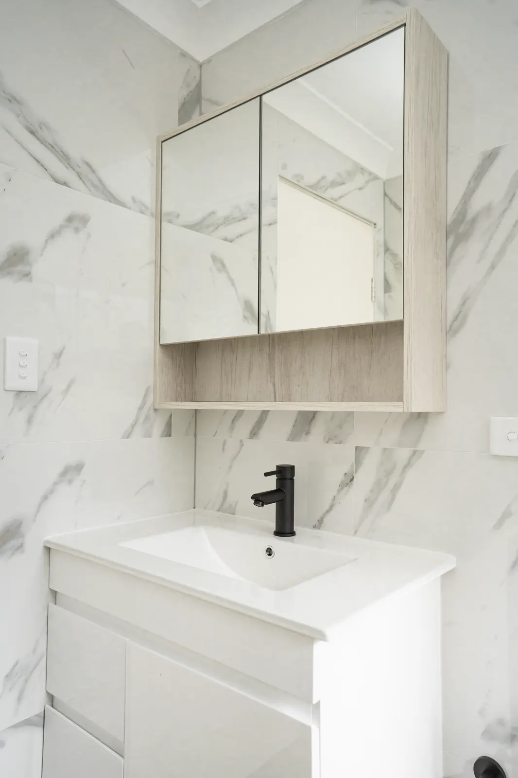 Vanity close-up — marble splashback with black mixer tap and timber mirror cabinet