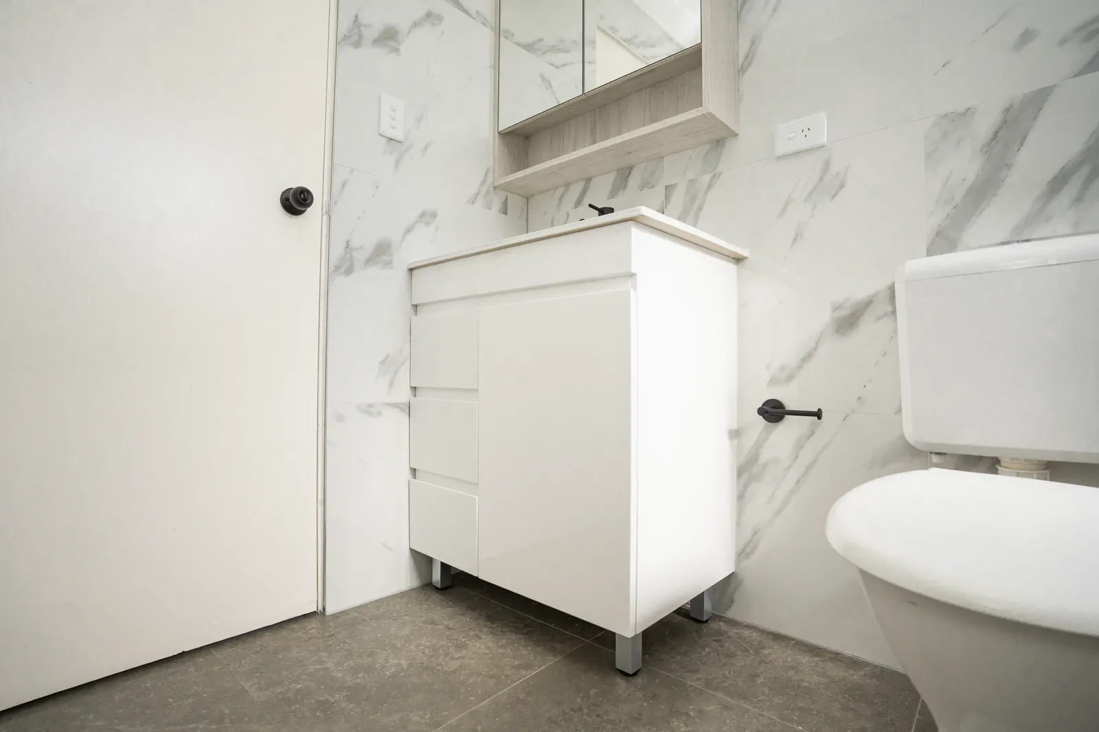 Full bathroom view from doorway — vanity, mirror cabinet, marble tiling