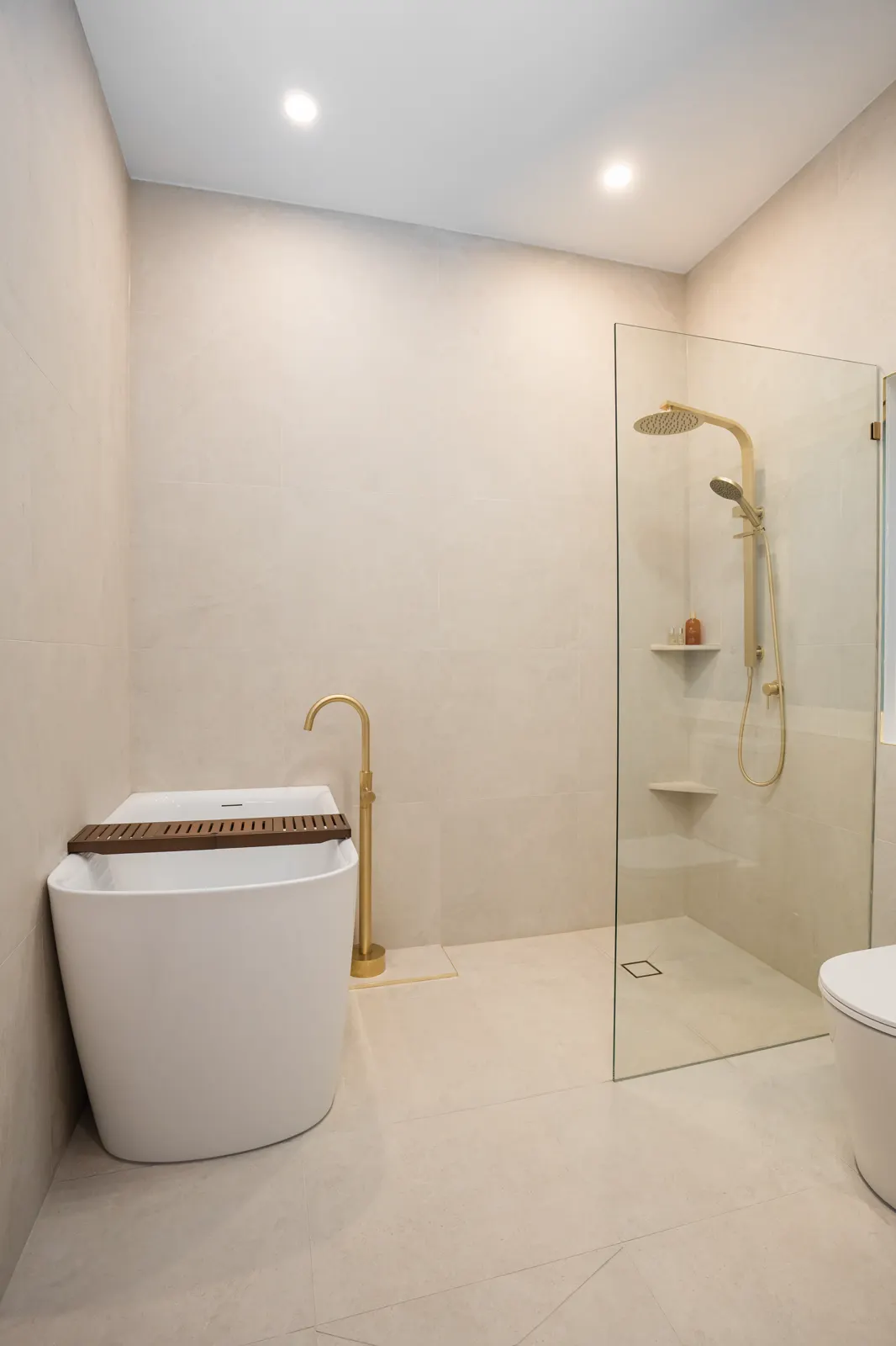 Bathroom overview — floor-to-ceiling porcelain tiling, frameless glass shower and freestanding tub